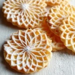 A stack of golden, lace-patterned pizzelle dusted with powdered sugar, showing the delicate texture and warm tones of this Classic Pizzelle Recipe.